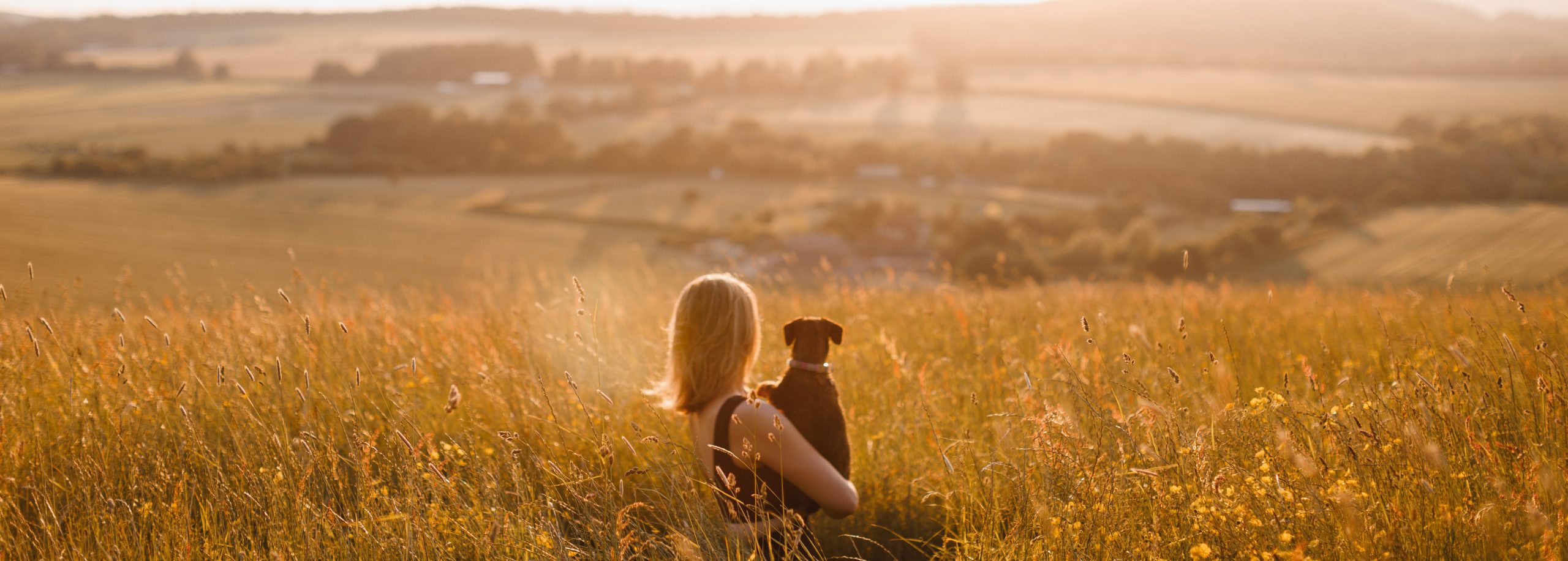 Lucy holding her dog in a field overlooking the countryside